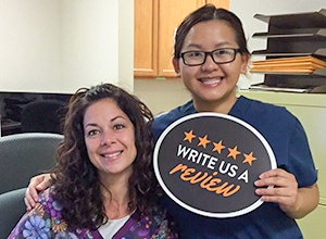 Dental team members smiling and holding a write a review sign